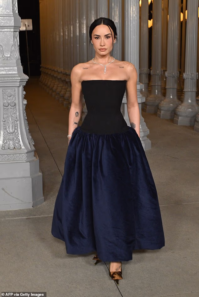 A slim-looking Demi Lovato departed from the celebratory outfits with a more formal midnight-blue off-the-shoulder gown